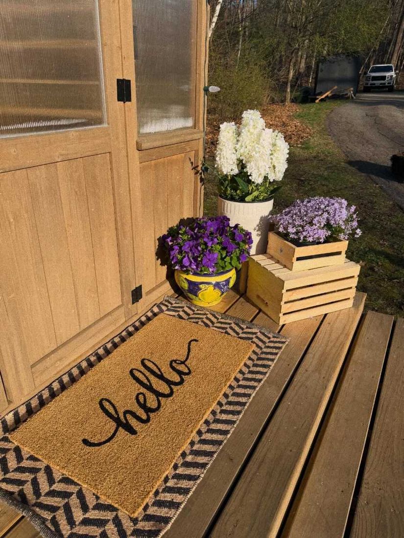 The sourdough shed door with a hello doormat and flowers